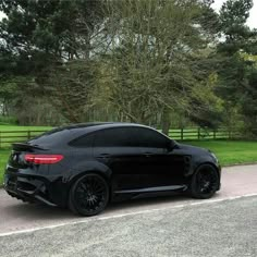 the black car is parked on the side of the road in front of some trees