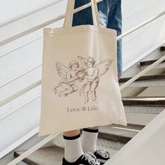 a person holding a tote bag that says love and life with two cherubs on it