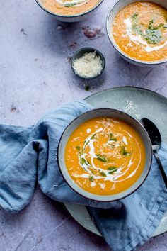 three bowls of carrot soup on a plate with spoons and blue napkin next to them