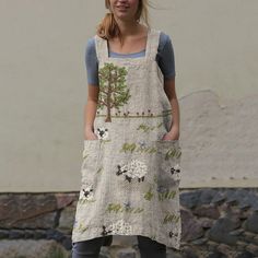 a woman standing in front of a stone wall wearing a dress with sheep on it