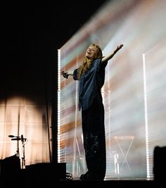 a woman standing on top of a stage holding her arms out to the side while singing