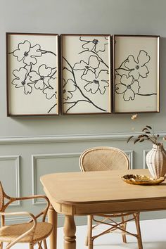 a dining room table with chairs and pictures on the wall above it, along with two vases filled with flowers