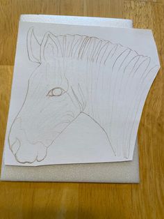 a piece of paper with a drawing of a horse's head on it sitting on top of a wooden table