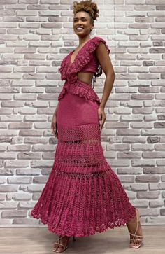 a woman standing in front of a brick wall wearing a pink dress with ruffles