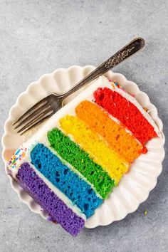 a slice of rainbow cake on a paper plate with a knife and fork next to it