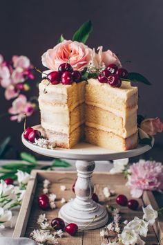 a cake with flowers and cherries on top sitting on a table next to a piece of cake