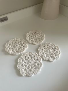 four crocheted coasters sitting on top of a white counter next to a vase