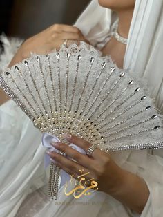 a woman in a white dress holding a hand fan with beads and pearls on it