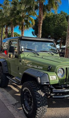 a green jeep is parked on the side of the road with palm trees in the background