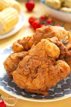 some fried food on a plate with corn and tomatoes in the backgroung