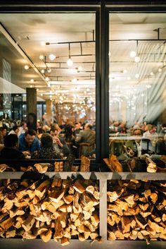 people sitting at tables in a restaurant with lots of wood stacked on top of each other