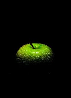 an apple with drops of water on it in the dark, against a black background