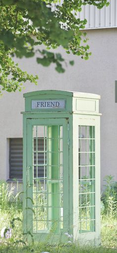 a green phone booth sitting in the grass next to a building with a sign that reads friend