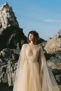 a woman in a wedding dress standing on rocks with her veil draped over her head