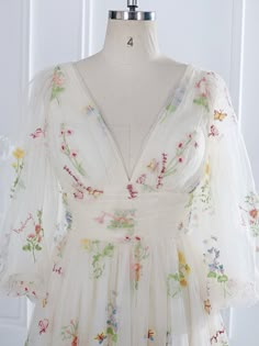 a white dress with colorful flowers on it is sitting on a mannequin head