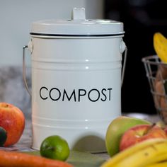 a white compost can sitting next to some fruit and vegetables