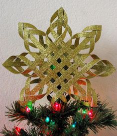 an ornament made out of gold paper on top of a christmas tree with lights