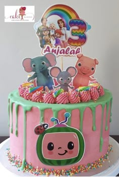 a pink and green birthday cake with animals on it's top, surrounded by sprinkles