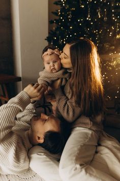 a woman holding a baby in her lap while laying on the floor next to a christmas tree