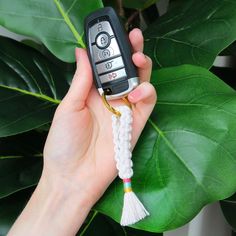 a hand holding a cell phone with a tassel on it's end and a keychain attached to it