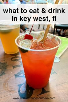 an orange drink in a plastic cup with a straw and cherry on the rim next to two drinks