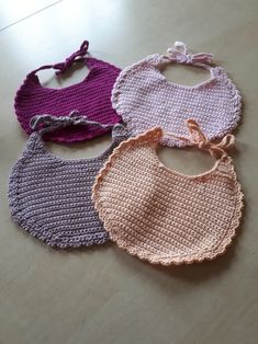 four crocheted bibs are sitting on a table together, one is pink, the other is purple