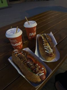 two hot dogs with toppings and drinks on a picnic table