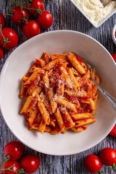 a plate of pasta with sauce and tomatoes on the table next to some utensils