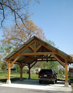 a car is parked under a wooden covered structure in the middle of a park area