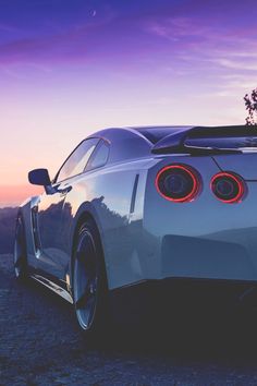 the rear end of a white sports car parked on top of a hill at sunset