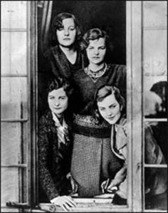 an old black and white photo of four women standing in front of a window with their arms around each other