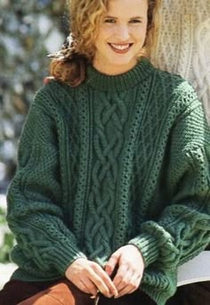 a woman sitting on a bench wearing a green cabled sweater and brown suede boots