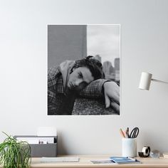 a black and white photo of a woman leaning her head on the wall next to a desk