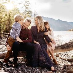 a family sitting on a log by the water