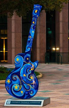 a blue guitar sculpture sitting on top of a cement slab in front of a building