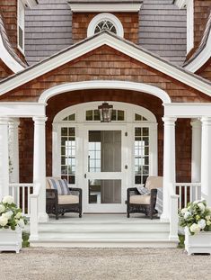 two chairs sitting on the front porch of a house with white pillars and windows,