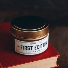 a book with a candle on top of it sitting next to a small container that says first edition