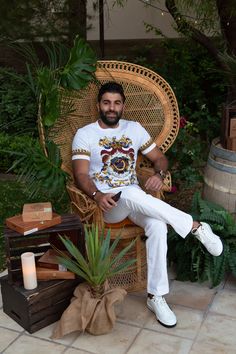 a man sitting in a wicker chair next to a potted plant