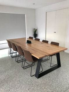 a large wooden table sitting in front of a white wall with chairs around it and a potted plant on top