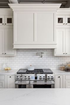 a white kitchen with marble counter tops and stainless steel stove top oven in the center