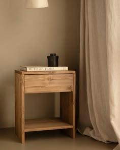 a small wooden table with a book on top and a lamp next to it in front of a window