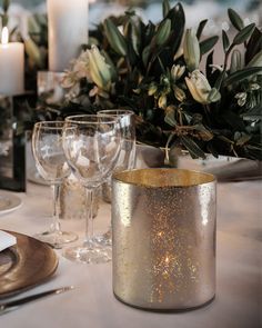 the table is set with candles, wine glasses and greenery in silver vases