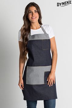 a woman standing wearing an apron and smiling at the camera with her hands in her pockets