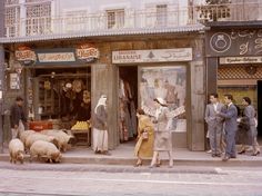 an old photo of people and sheep in front of a store on a street corner