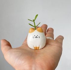 a hand holding a small ceramic cat with a plant in it's mouth,