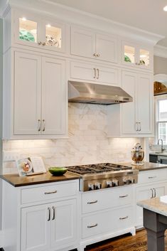 a kitchen with white cabinets and marble counter tops, an oven hood over the stove