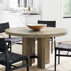 a bowl on top of a wooden table in a white room with black leather chairs