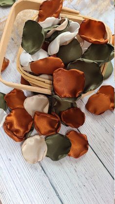 several pieces of cloth flowers in a basket on a white wooden table with green leaves