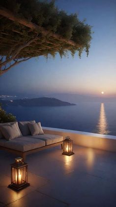 an outdoor seating area overlooking the ocean at night with lanterns lit up in front of it