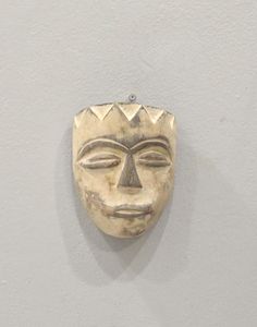 a wooden mask hanging on the wall in front of a white wall with a gray background